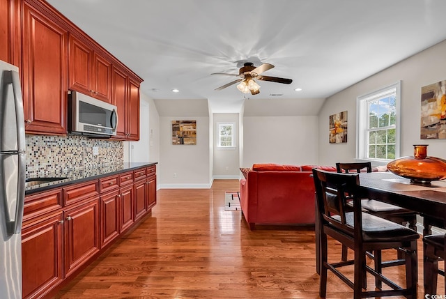 kitchen featuring ceiling fan, backsplash, dark countertops, wood finished floors, and stainless steel appliances