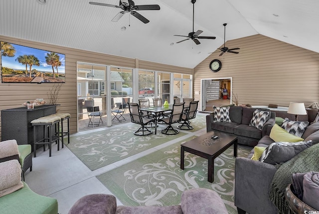living area featuring concrete flooring, ceiling fan, wooden walls, and high vaulted ceiling