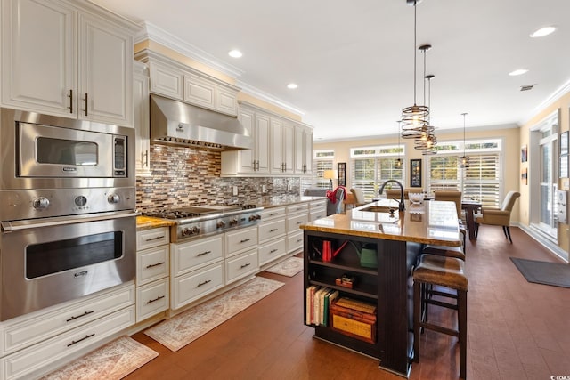 kitchen featuring crown molding, wall chimney range hood, a kitchen bar, stainless steel appliances, and a sink