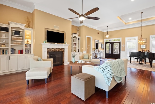 living room featuring visible vents, dark wood finished floors, ornamental molding, a stone fireplace, and ceiling fan with notable chandelier