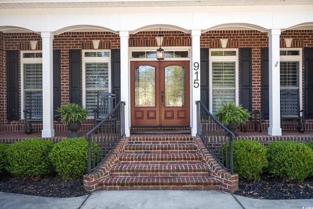 view of exterior entry with a porch, french doors, and brick siding