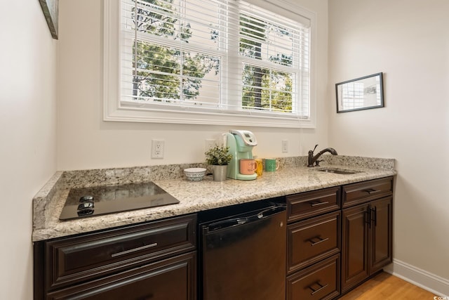 bar featuring light wood finished floors, black appliances, baseboards, and a sink