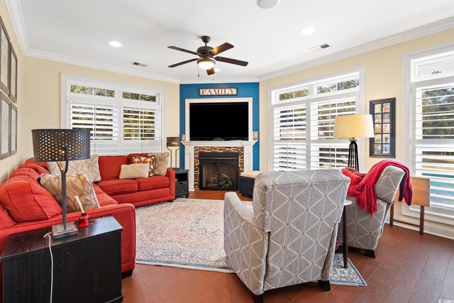 living area featuring wood-type flooring, a stone fireplace, ceiling fan, and crown molding