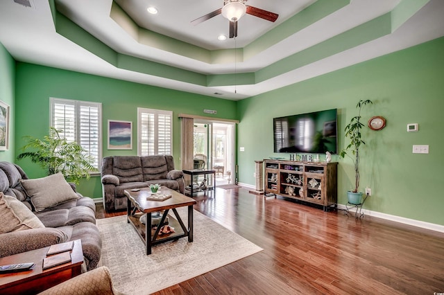 living area featuring baseboards, a ceiling fan, a tray ceiling, and wood finished floors