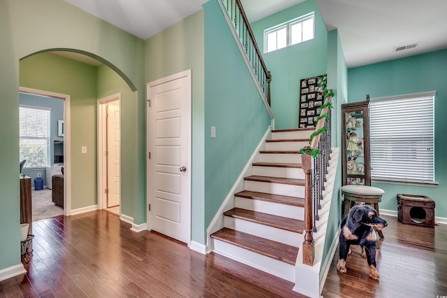 stairs featuring a wealth of natural light, baseboards, arched walkways, and wood-type flooring