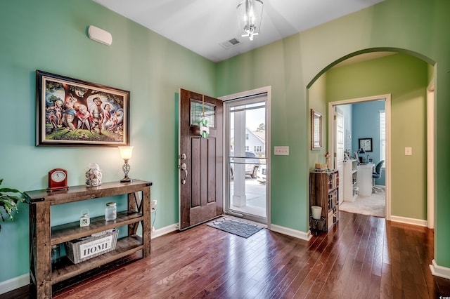 foyer featuring arched walkways, visible vents, baseboards, and dark wood-style floors