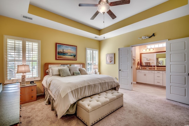 bedroom featuring light carpet, visible vents, ensuite bath, and a tray ceiling