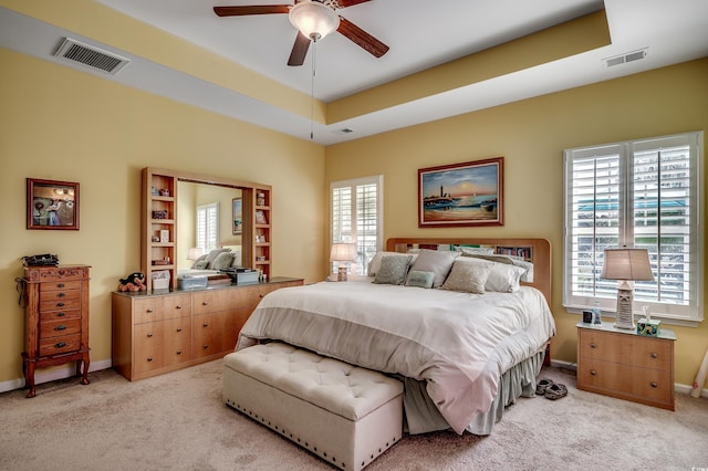 bedroom with a raised ceiling, light colored carpet, and visible vents