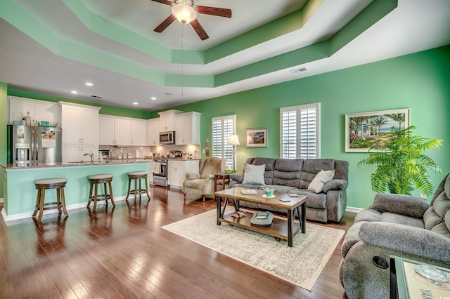 living room with visible vents, dark wood-type flooring, baseboards, a raised ceiling, and a ceiling fan