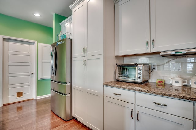 kitchen with dark stone counters, tasteful backsplash, light wood-style flooring, and freestanding refrigerator