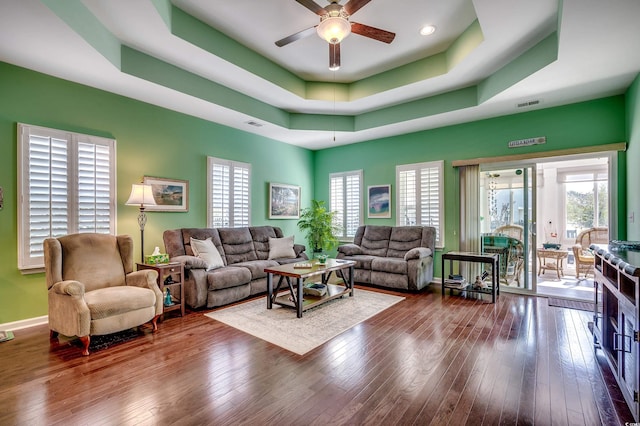 living area with a tray ceiling, a ceiling fan, visible vents, and wood-type flooring