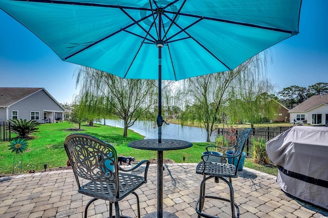 view of patio with a grill, fence, and a water view