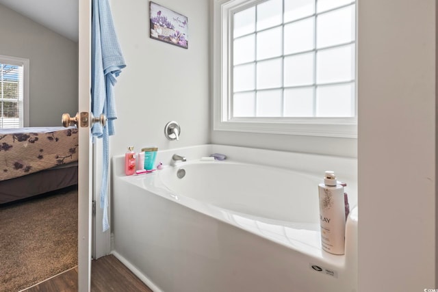 ensuite bathroom featuring connected bathroom, wood finished floors, and a bath