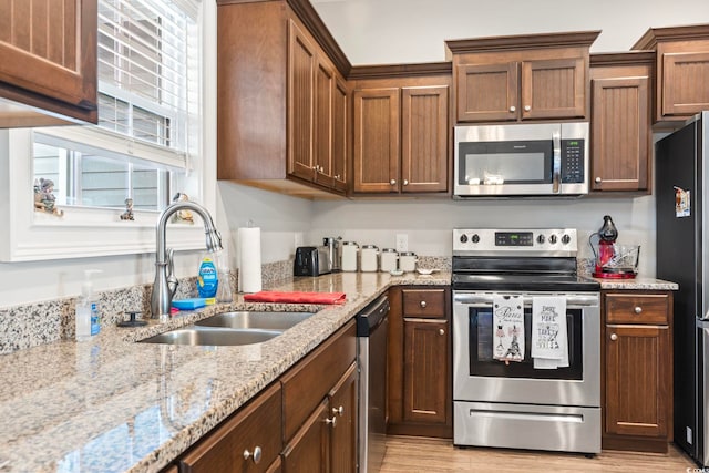 kitchen featuring a sink, stainless steel appliances, light stone counters, and light wood-type flooring