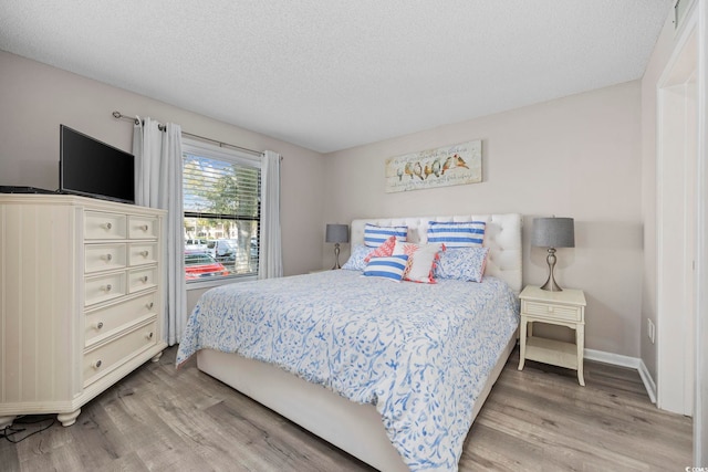 bedroom with a textured ceiling, baseboards, and light wood-style flooring