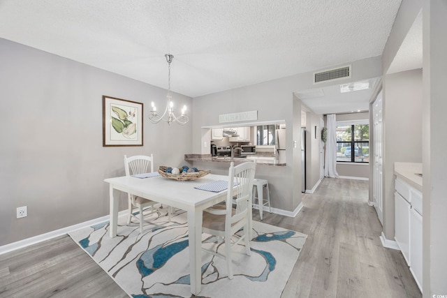 dining area featuring visible vents, light wood finished floors, baseboards, and a chandelier