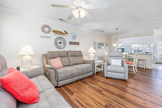 living area with visible vents, a ceiling fan, a textured ceiling, wood finished floors, and crown molding