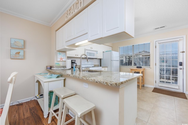 kitchen featuring visible vents, crown molding, light stone counters, a peninsula, and white appliances