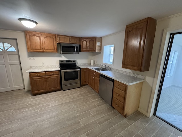 kitchen with light countertops, crown molding, brown cabinetry, appliances with stainless steel finishes, and a sink