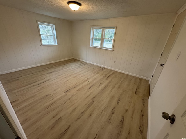 empty room featuring light wood-style floors, wooden walls, a textured ceiling, and a wealth of natural light