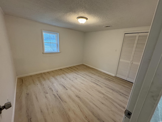 unfurnished bedroom featuring a closet, baseboards, a textured ceiling, visible vents, and wood finished floors