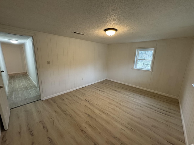 spare room featuring visible vents, a textured ceiling, baseboards, and wood finished floors