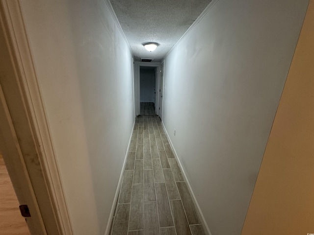 hallway featuring a textured ceiling, visible vents, baseboards, and wood tiled floor