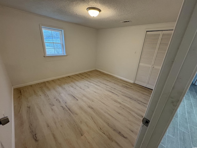 unfurnished bedroom with visible vents, baseboards, a closet, a textured ceiling, and wood finished floors