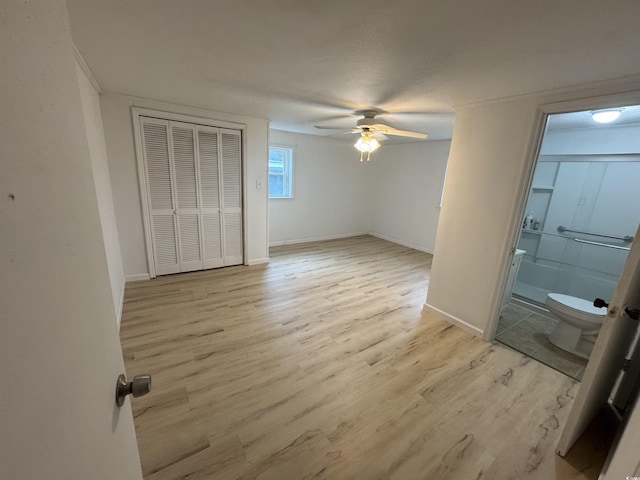 unfurnished bedroom with light wood-type flooring, baseboards, a ceiling fan, and ensuite bath