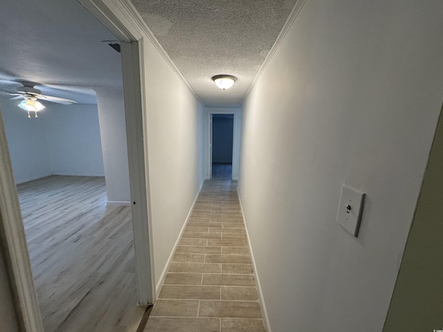 hallway featuring a textured ceiling, wood finished floors, baseboards, and ornamental molding