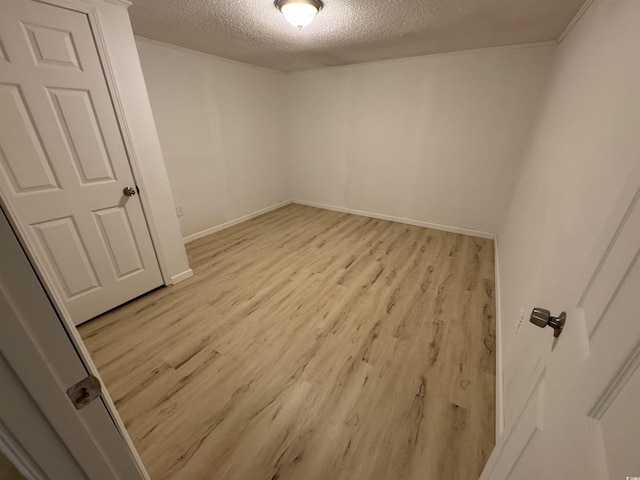 spare room featuring baseboards, light wood-type flooring, and a textured ceiling