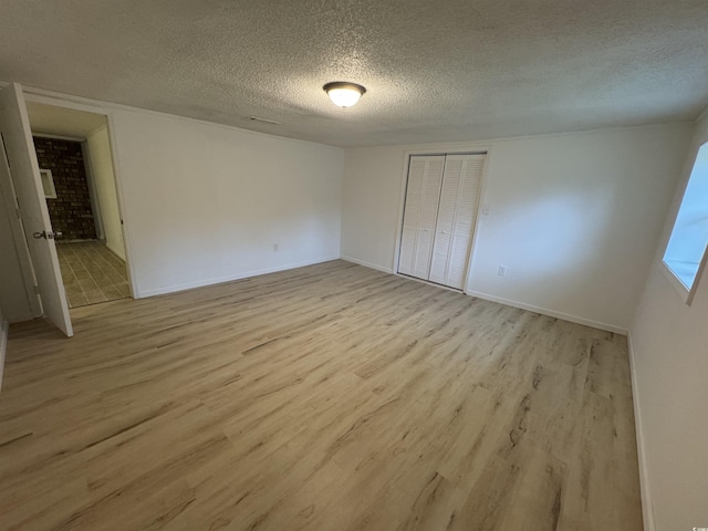 unfurnished bedroom featuring a closet, light wood-style flooring, baseboards, and a textured ceiling
