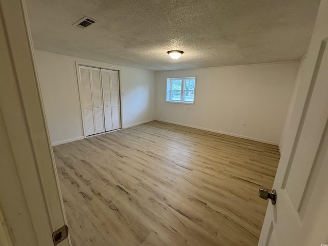 unfurnished bedroom with light wood-style flooring, a textured ceiling, a closet, visible vents, and baseboards