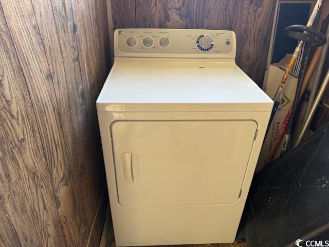 clothes washing area with wood walls, washer / clothes dryer, and laundry area