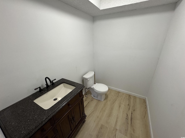 half bath with toilet, vanity, wood finished floors, and baseboards