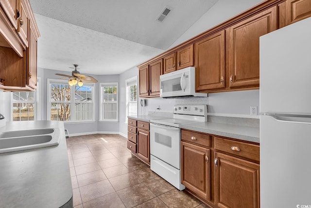 kitchen with white appliances, brown cabinetry, dark tile patterned flooring, visible vents, and a sink