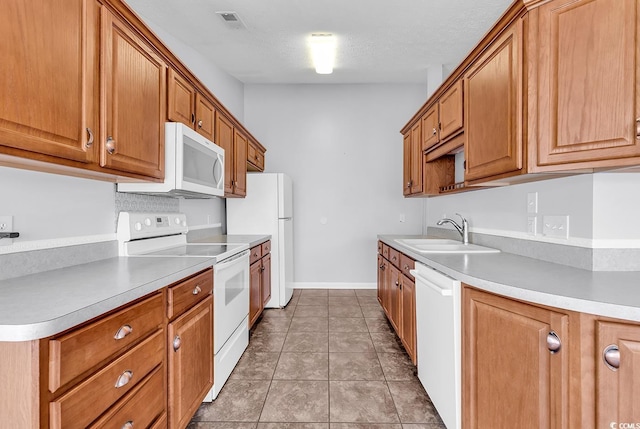 kitchen featuring visible vents, a sink, light countertops, white appliances, and brown cabinetry