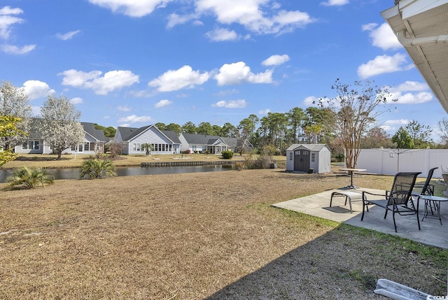 view of yard featuring a patio, an outdoor structure, a water view, fence, and a storage unit