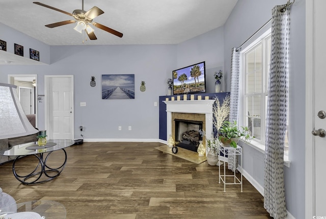 living area featuring a tiled fireplace, a ceiling fan, baseboards, and wood finished floors