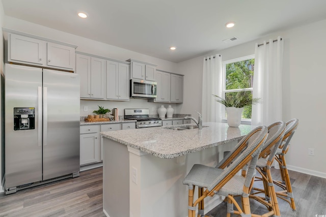 kitchen with stainless steel appliances, a sink, wood finished floors, gray cabinets, and light stone countertops