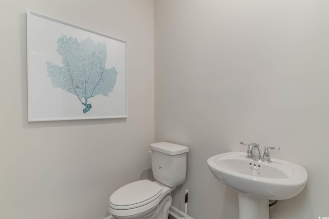 half bath with toilet, a sink, and baseboards