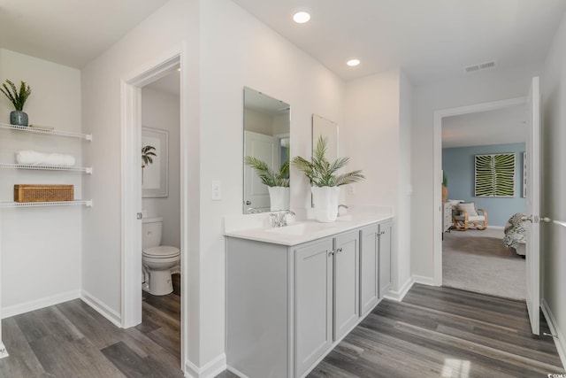 ensuite bathroom with wood finished floors, double vanity, toilet, baseboards, and recessed lighting