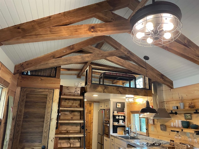 kitchen featuring wooden walls, lofted ceiling with beams, a sink, stainless steel oven, and wall chimney exhaust hood