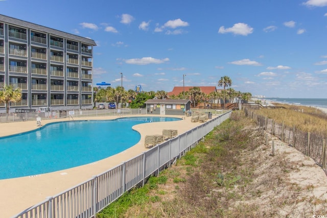 community pool with fence, a patio area, and a water view