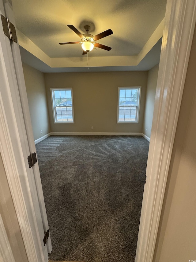 spare room with baseboards, a raised ceiling, and dark carpet