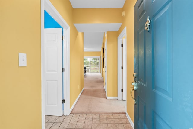 hall featuring baseboards, light carpet, and light tile patterned floors