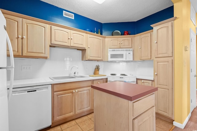 kitchen featuring visible vents, a sink, light brown cabinets, and white appliances