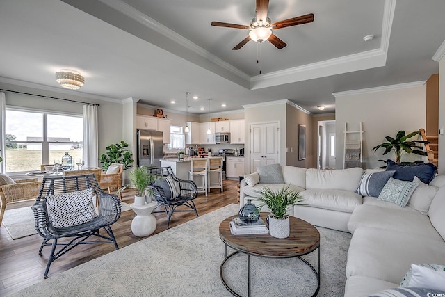 living room with a tray ceiling, crown molding, wood finished floors, and a ceiling fan