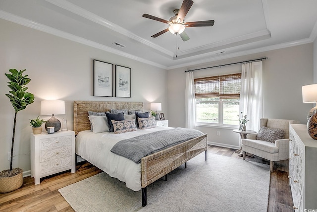 bedroom featuring baseboards, hardwood / wood-style flooring, a tray ceiling, and crown molding