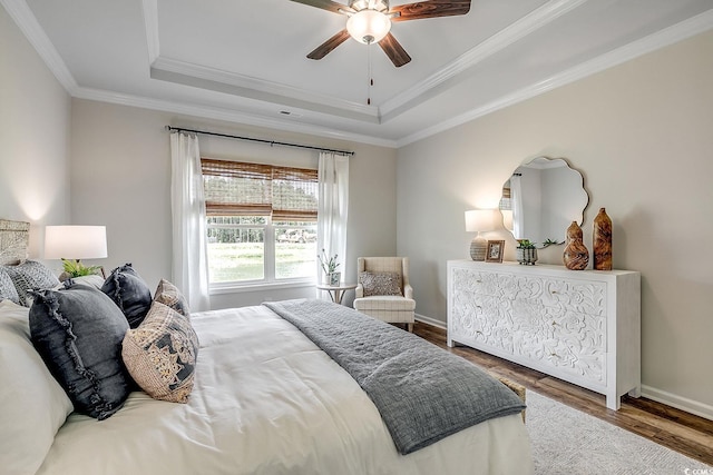 bedroom featuring baseboards, wood finished floors, a raised ceiling, and crown molding